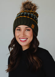 Woman wearing a green knit beanie with a pom-pom against a plain background