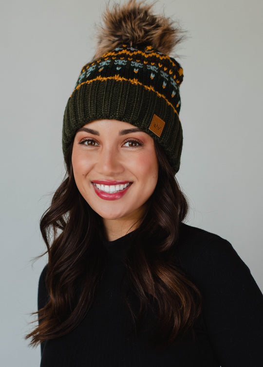Woman wearing a green knit beanie with a pom-pom against a plain background