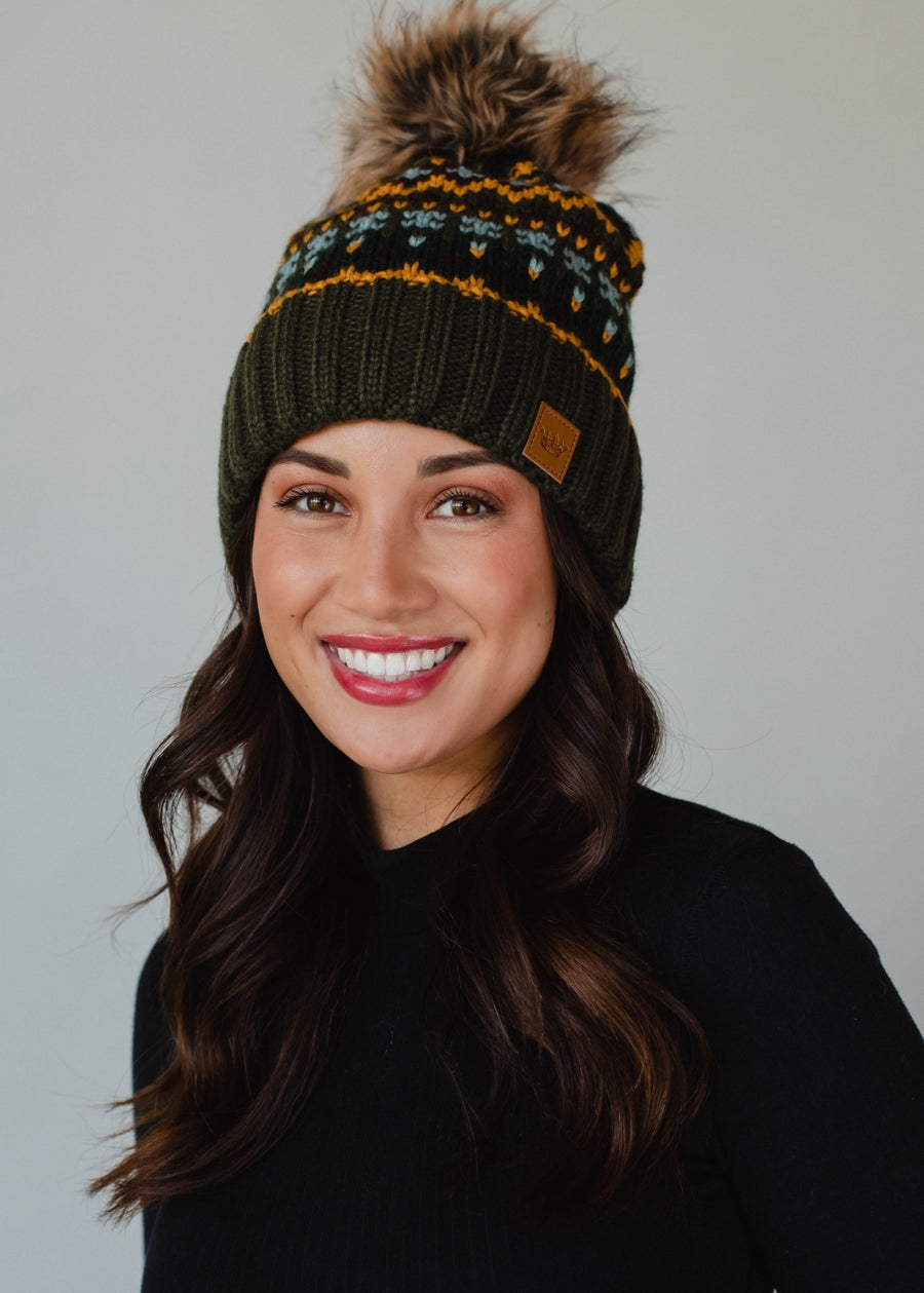 Woman wearing a green knit beanie with a pom-pom against a plain background