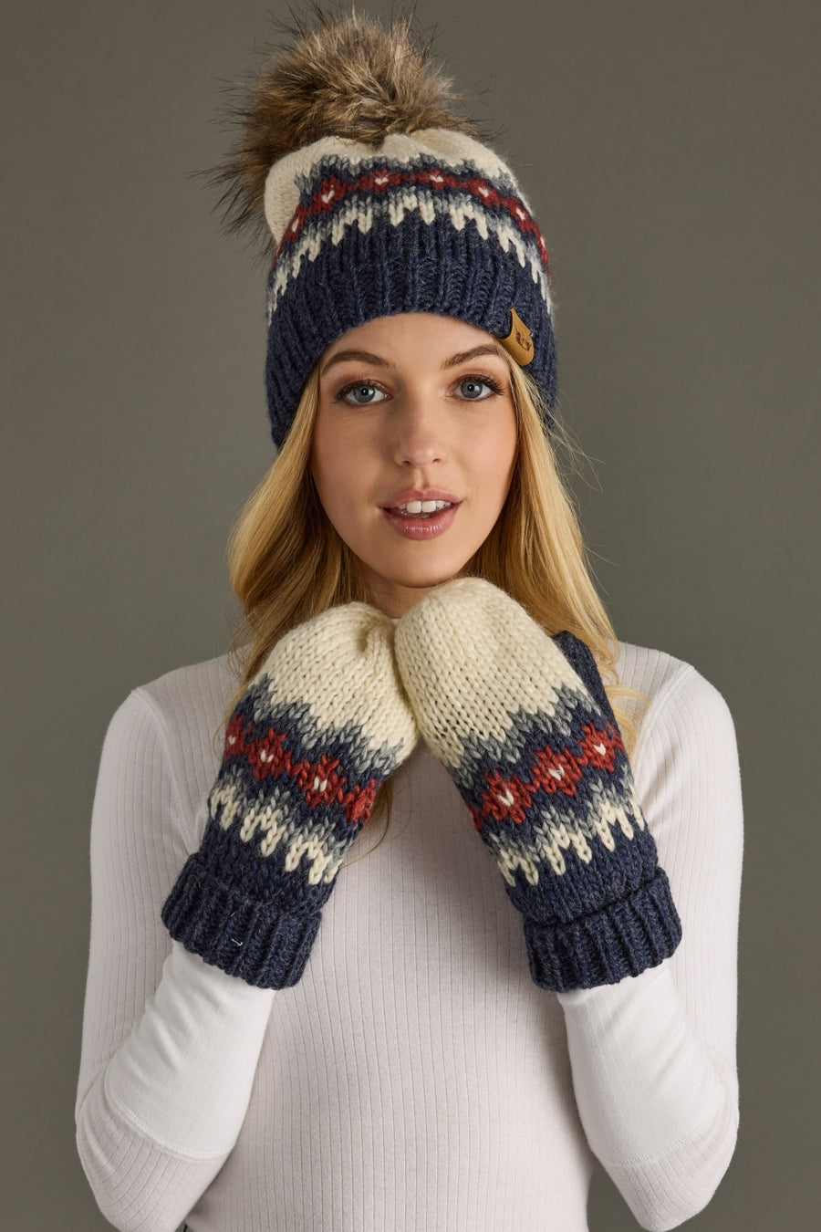 Woman wearing a knit hat and mittens with a pattern on a gray background