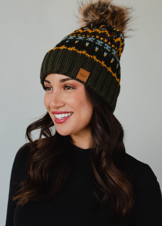 Woman wearing a patterned beanie with a pom-pom on a gray background