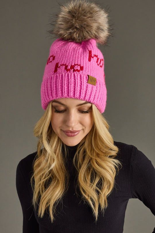 Person wearing a pink beanie with a fur pom-pom on a gray background