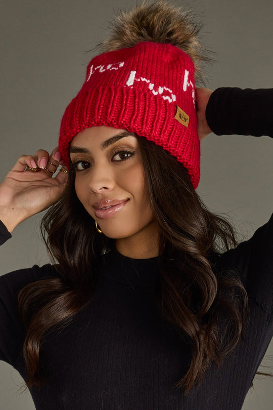 Woman wearing a red knit beanie with a pom-pom against a neutral background