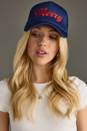 Woman wearing a blue cap with 'Merry' embroidered on it against a gray background