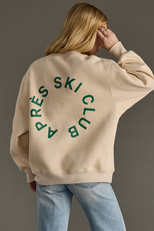 Person wearing a beige sweatshirt with green text on the back against a gray background