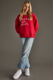 Woman wearing a red sweatshirt with text, blue jeans, and white sneakers on a gray background