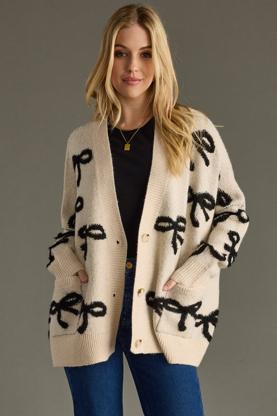 Woman wearing a cream cardigan with black patterns on a gray background