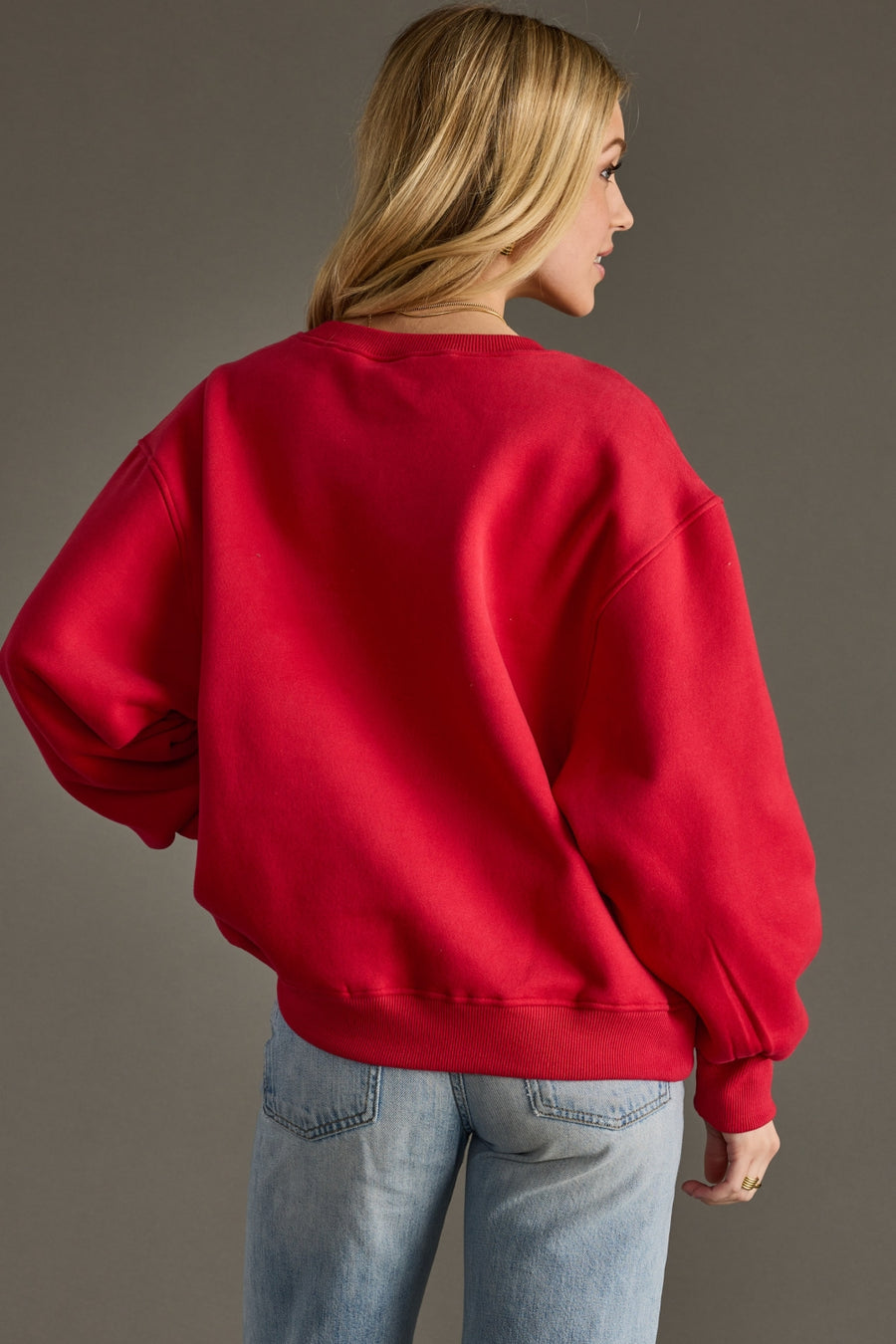 Person wearing a red sweatshirt and blue jeans against a gray background