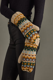 Pair of patterned mittens held by a person wearing black sleeves and pants against a gray background