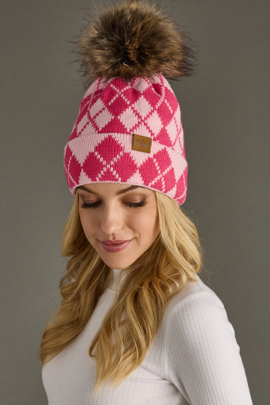 Pink and blush argyle beanie with a pom-pom worn by a person on a gray background