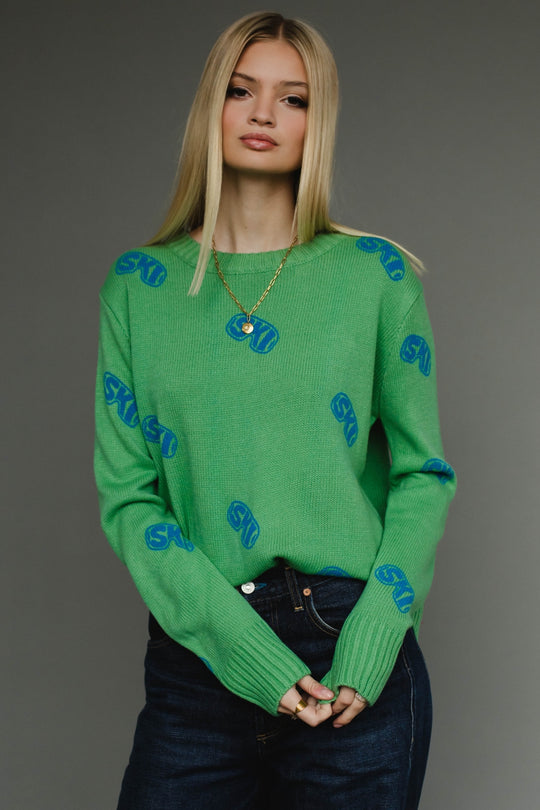 Woman wearing a green sweater with blue patterns against a gray background