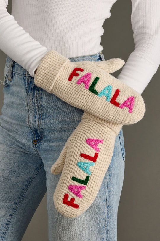 Beige mittens with colorful 'FALALA' text worn by a person in jeans and a white sweater.