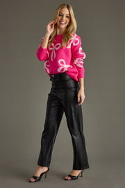 Woman wearing a pink sweater with white patterns and black pants on a gray background