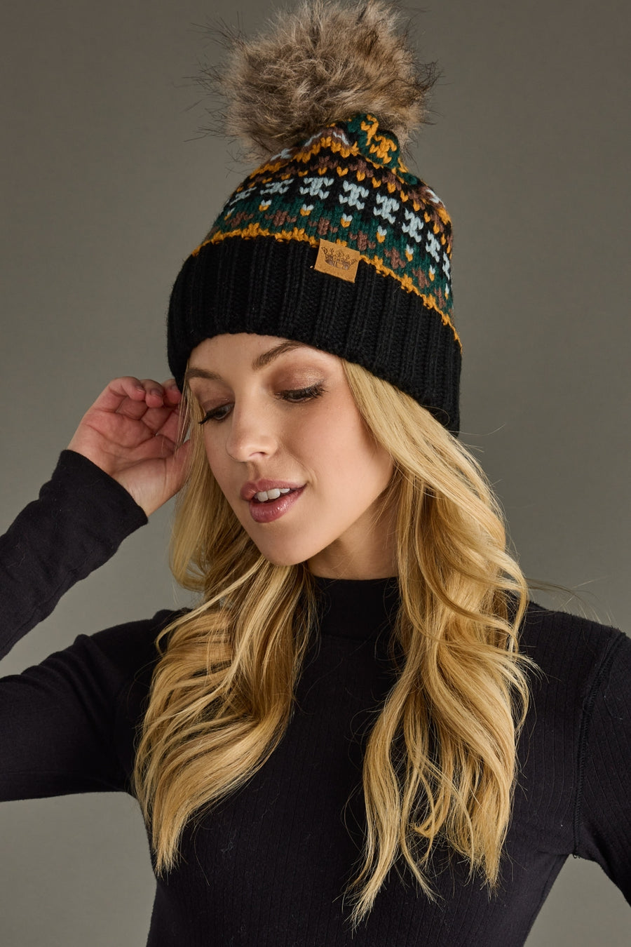 Woman wearing a patterned beanie with a pom-pom against a gray background