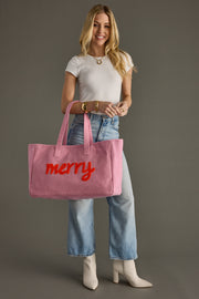 Woman holding a pink tote bag with 'merry' on it against a gray background