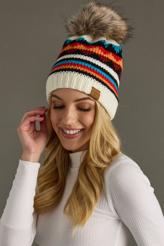 Woman wearing a colorful striped beanie with a pom-pom on a gray background