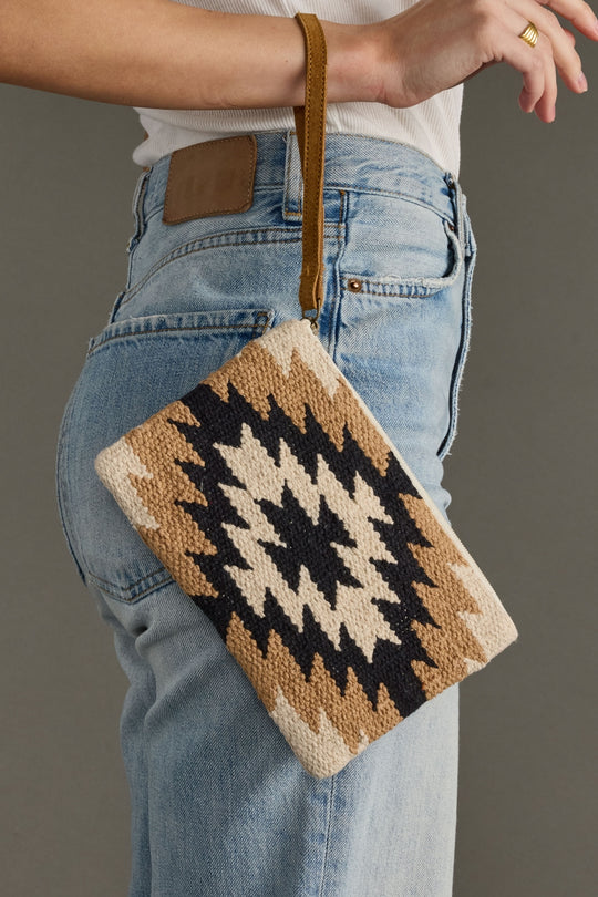 Person holding a patterned clutch bag with jeans and a plain background
