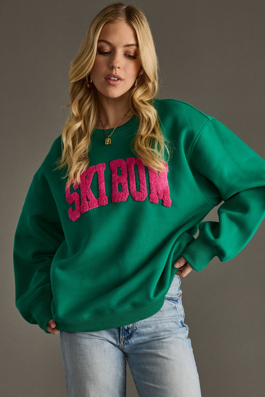 Woman wearing a green sweatshirt with pink text against a gray background