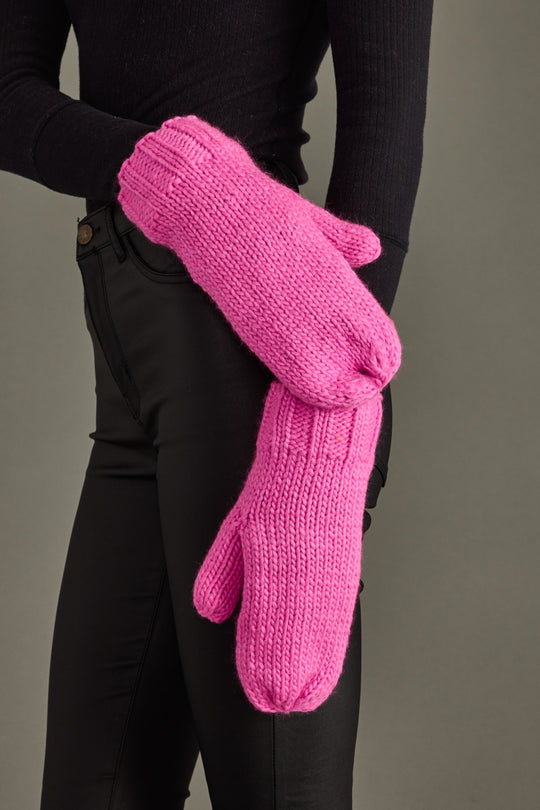Person wearing bright pink knitted mittens against a neutral background