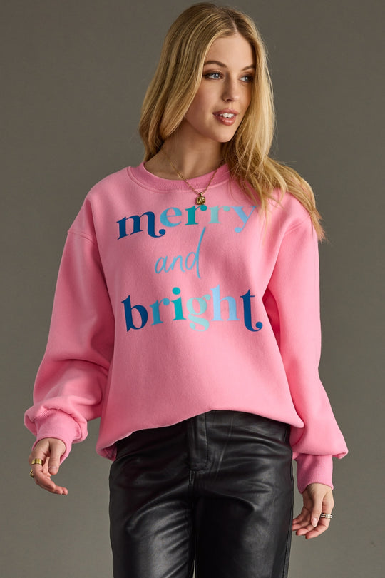 Woman wearing a pink sweatshirt with 'merry and bright' text on a gray background