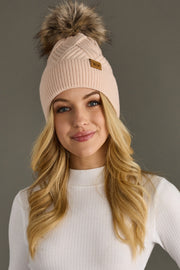 Woman wearing a pink knit beanie with a fur pom-pom on a gray background