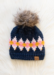 Navy knit beanie with colorful diamond pattern and fur pom-pom on a white background