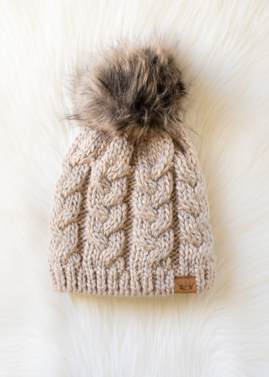 Beige knitted beanie with a fur pom-pom on a white background
