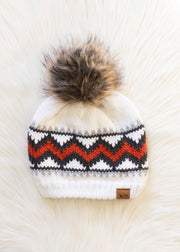 Knitted beanie with a fur pom-pom on a textured white background