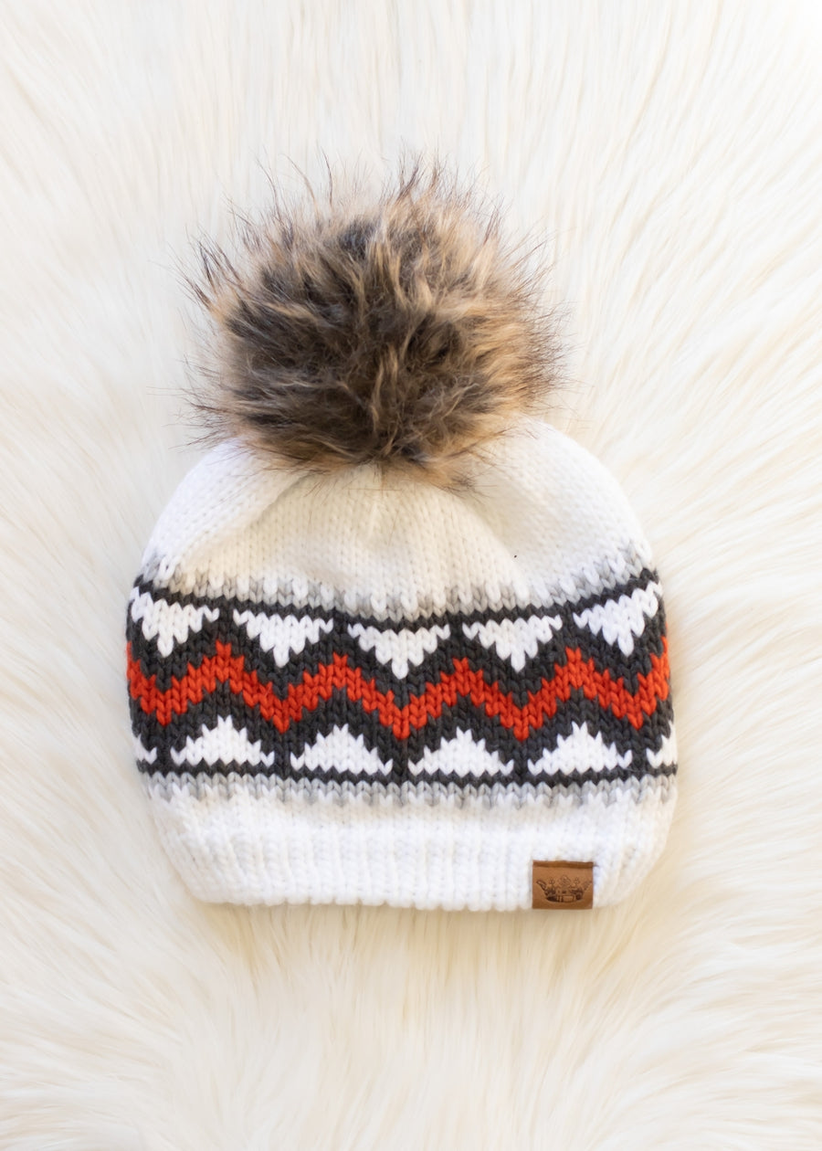Knitted beanie with a fur pom-pom on a textured white background