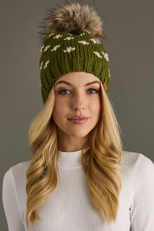Woman wearing a green knit beanie with a fur pom-pom against a gray background