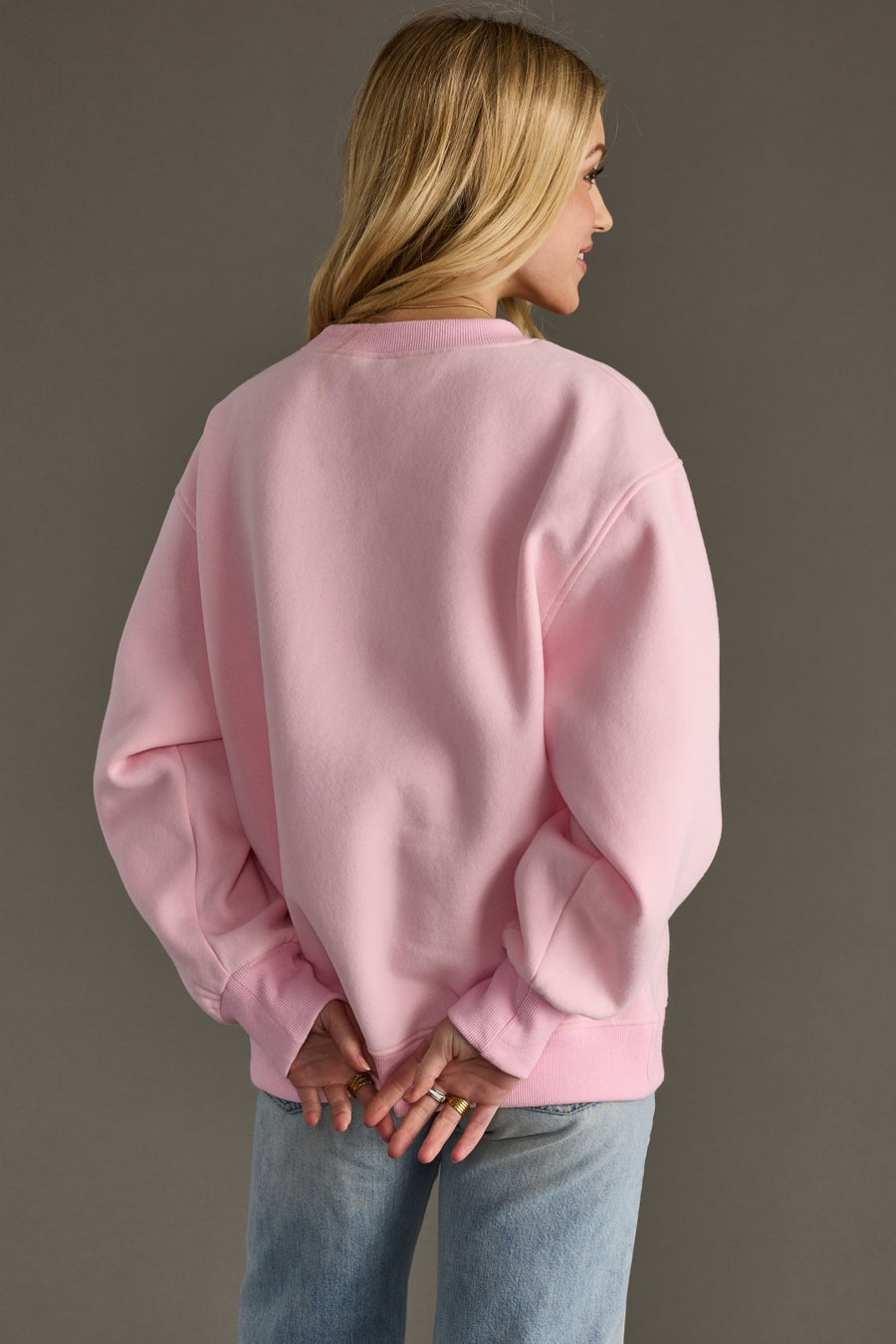 Person wearing a pink sweatshirt and blue jeans against a gray background