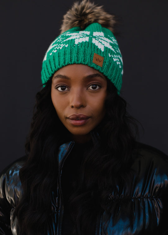 Person wearing a green knit beanie with a brand logo on a dark background