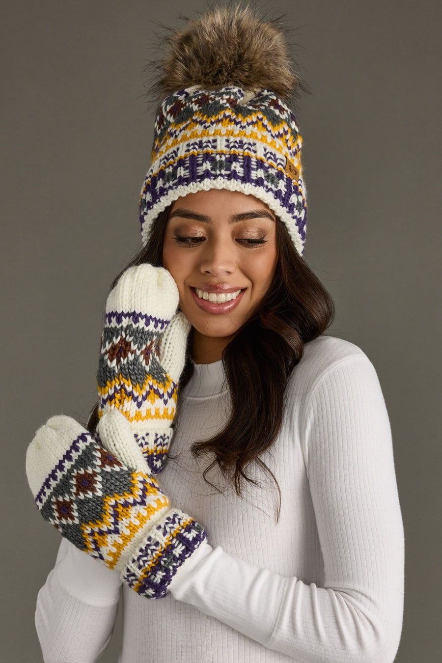 Woman wearing a patterned knit hat and mittens against a gray background