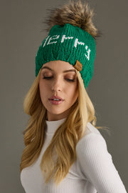 Woman wearing a green knit beanie with a fur pom-pom on a gray background