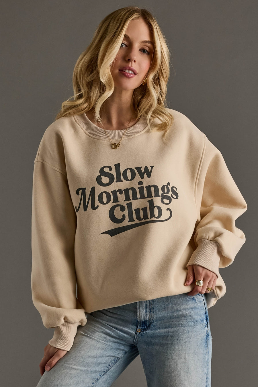 Woman wearing a beige sweatshirt with 'Slow mornings club' text on a gray background