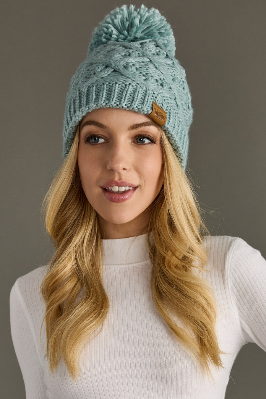 Woman wearing a teal knit beanie with a pom-pom against a neutral background