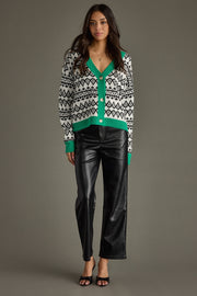 Woman wearing a patterned cardigan with green accents and black leather pants on a gray background