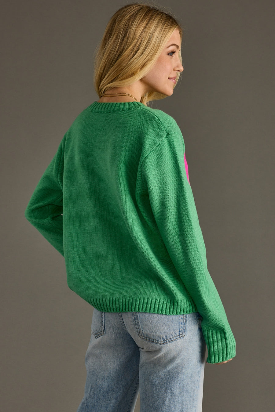 Person wearing a green sweater and light blue jeans against a gray background