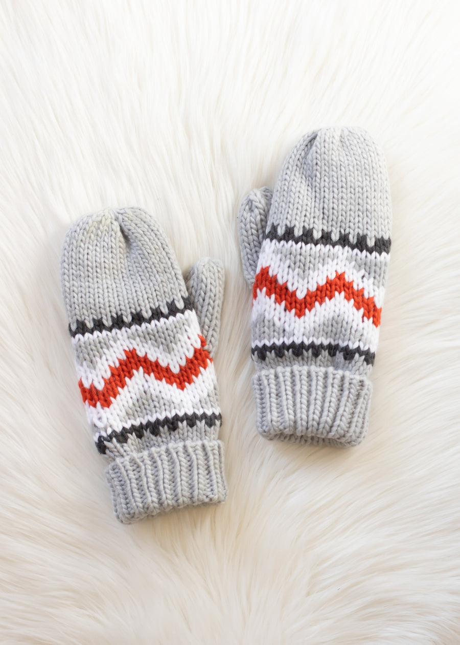 Pair of gray knitted mittens with red and white pattern on a fluffy white surface