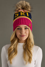 Woman wearing a colorful knit beanie with a pom-pom on a gray background