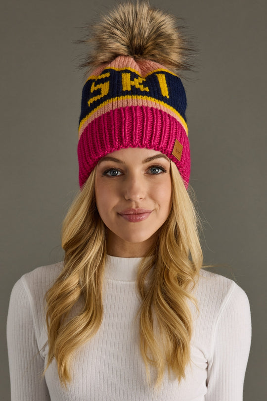 Woman wearing a colorful knit beanie with a pom-pom on a gray background