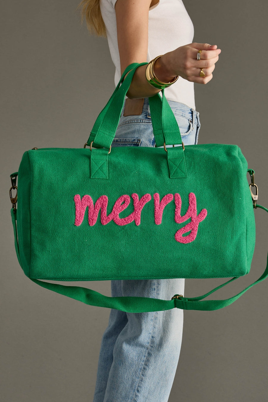 Green bag with 'merry' in pink text held by a person against a gray background