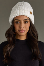Woman wearing a white knit beanie with a brand logo on a gray background