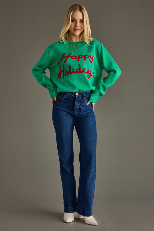 Person wearing a green sweater with 'Happy Holidays' text and blue jeans on a gray background