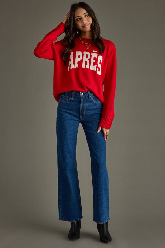 Woman wearing a red sweater with 'APRèS' text and blue jeans on a gray background