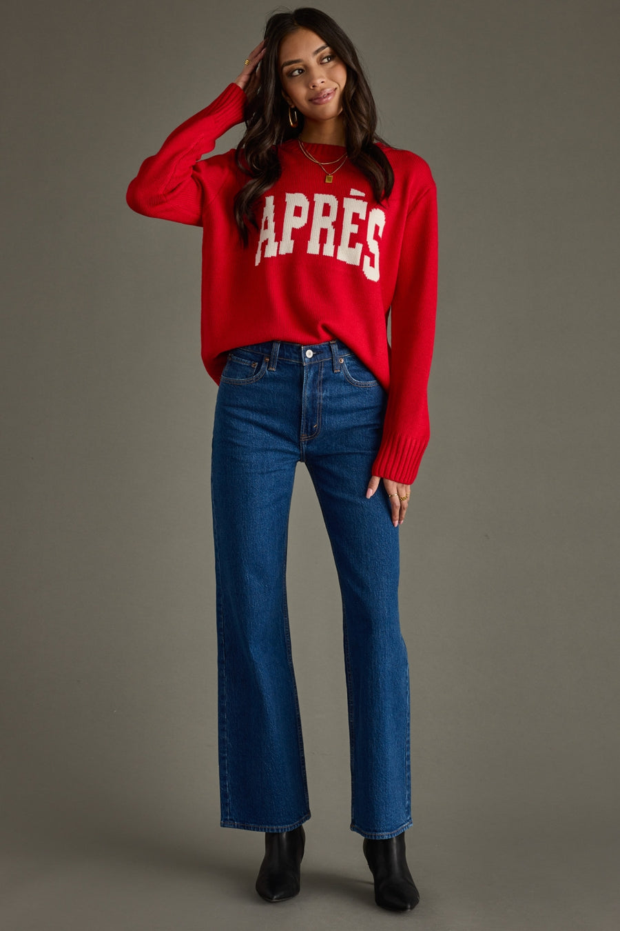 Woman wearing a red sweater with 'APRèS' text and blue jeans on a gray background