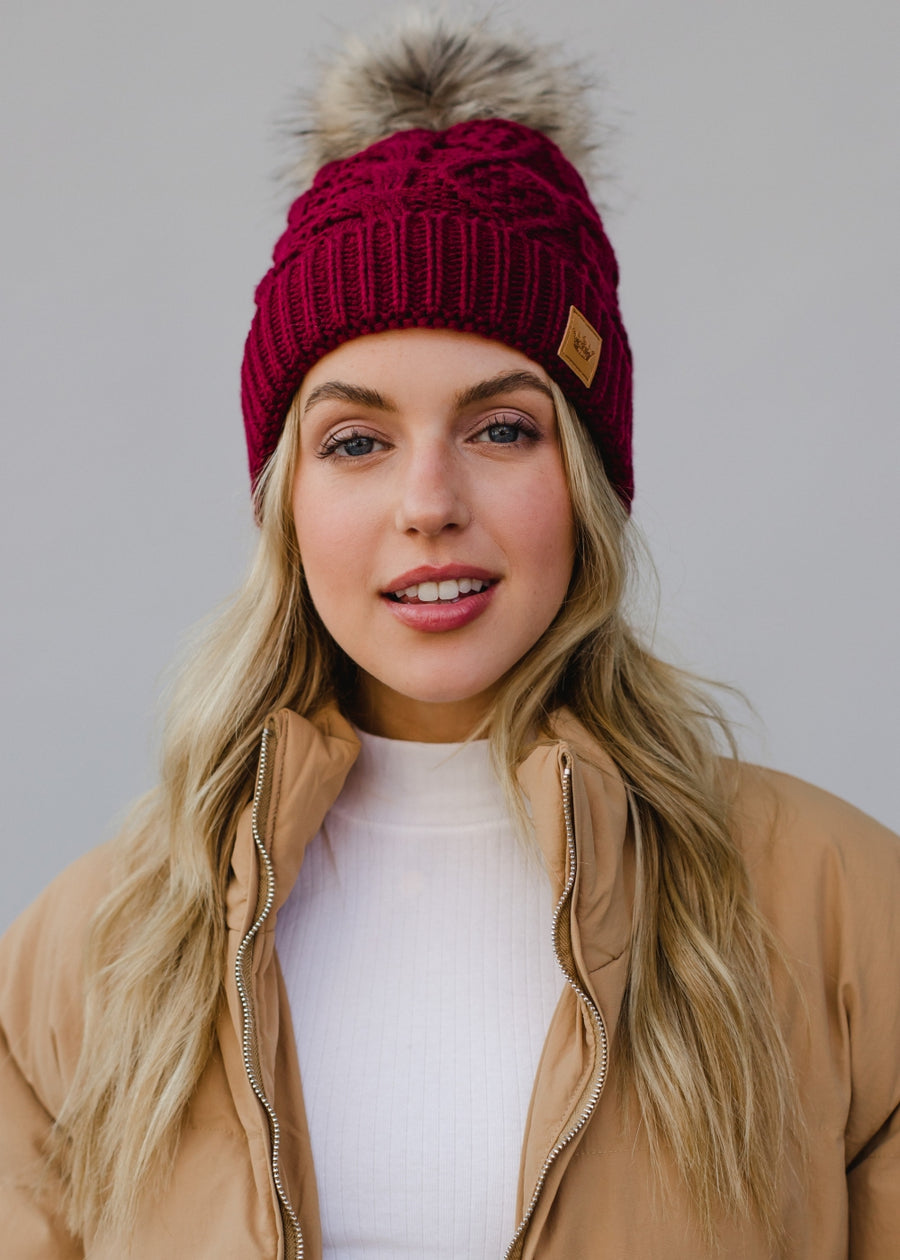 Woman wearing a red knit beanie with a fur pom-pom against a plain background