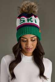 Woman wearing a colorful knit beanie with a pom-pom on a gray background