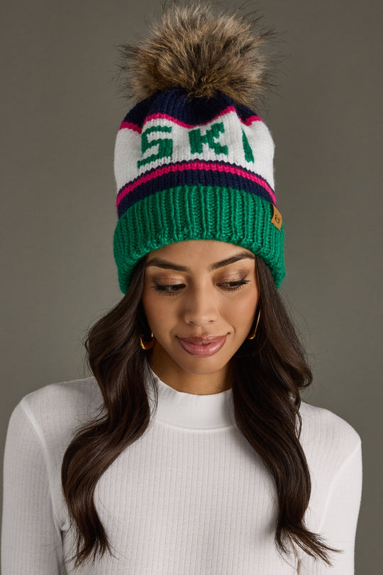 Woman wearing a colorful knit beanie with a pom-pom on a gray background