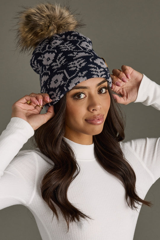 Woman wearing a patterned beanie with a pom-pom on a neutral background
